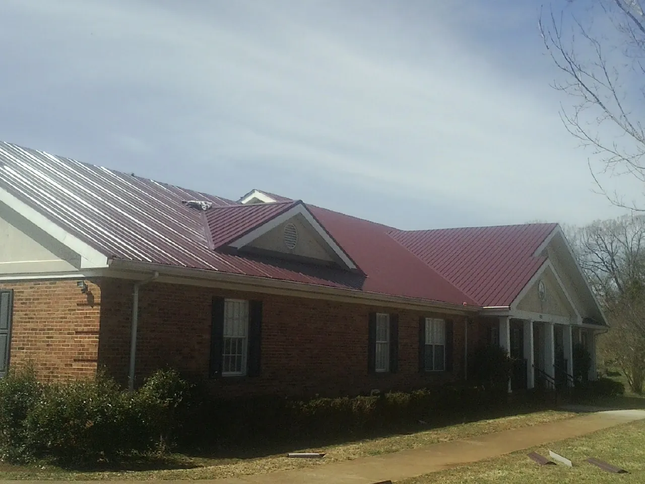 Red metal roof with gabled entries on a long brick building, from a Hail Damage Roof Repair job in Millersport