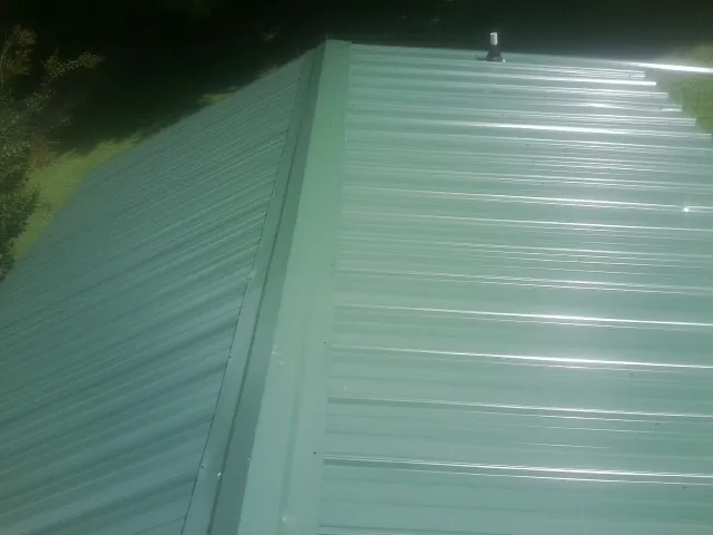 New green metal panels meeting at the ridge of a roof — Flat Roof Repair work by our crew in Millersport