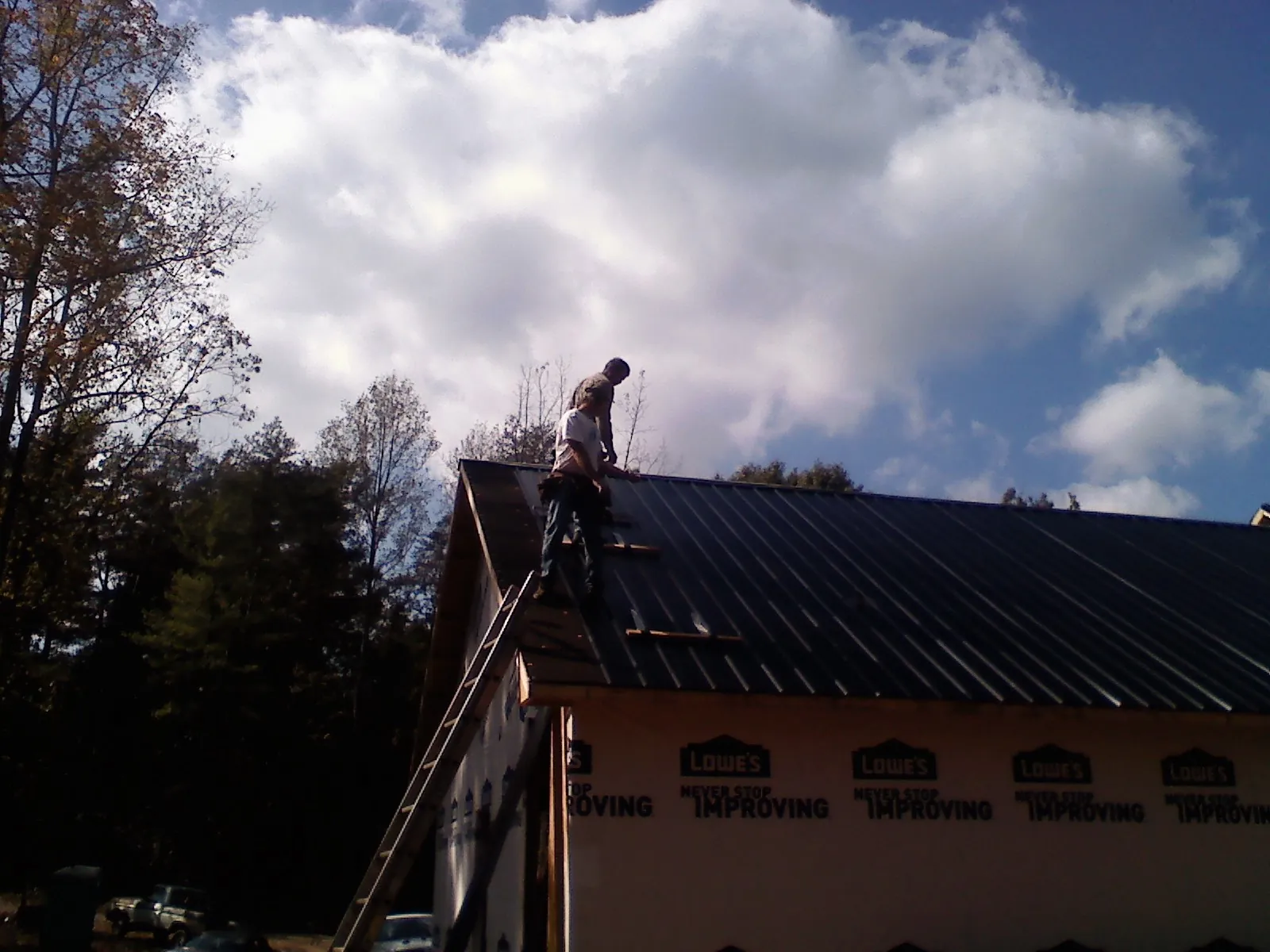 Roofer fastening dark metal panels high against a cloudy sky, from a Roof Inspection job in Millersport
