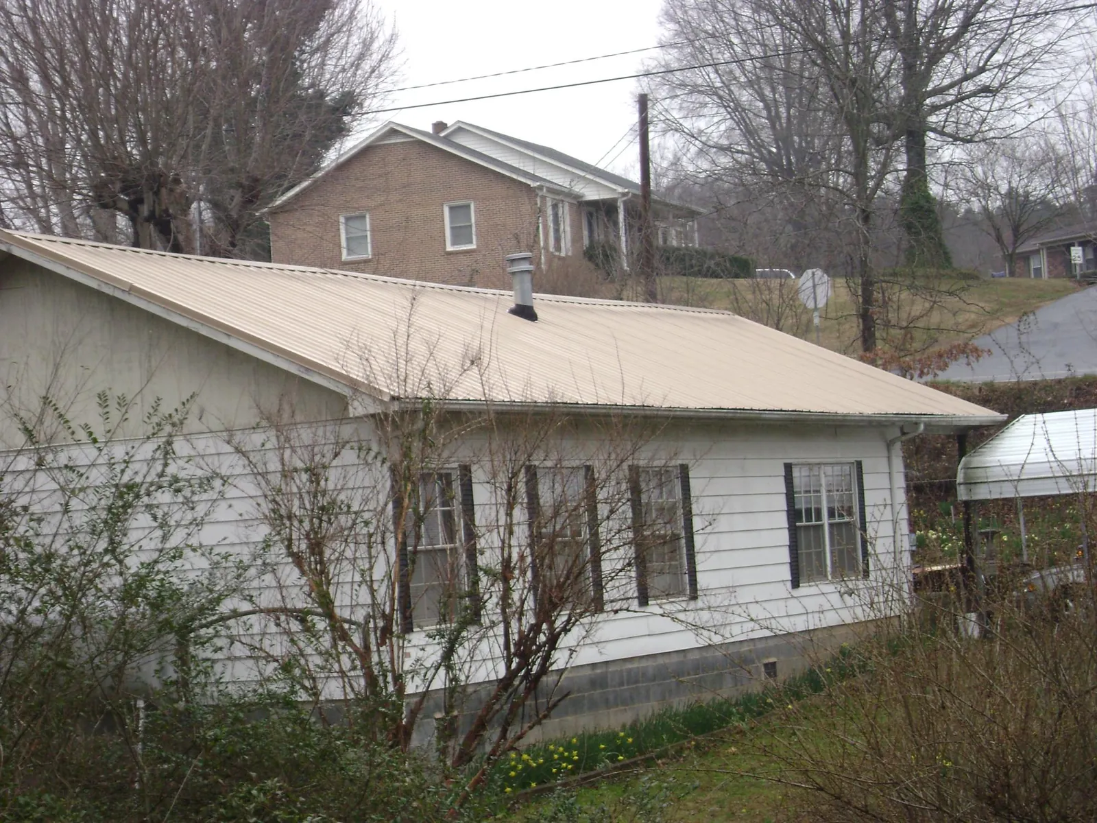 Tan metal roof on a white sided house set into a hillside — Commercial Roofing by Roofing Brothers in Millersport